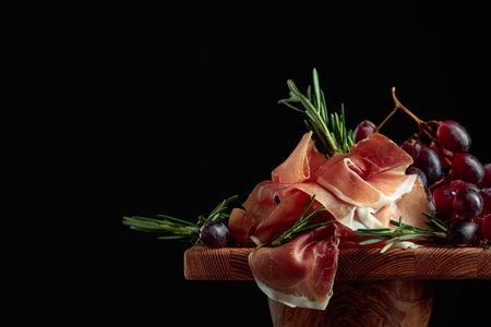 Prosciutto with grapes and rosemary on a black background. Copy space.の写真素材