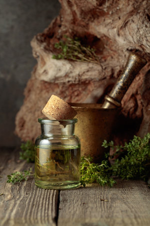 Bottle of thyme essential oil with fresh thyme twigs on an old wooden table.の写真素材