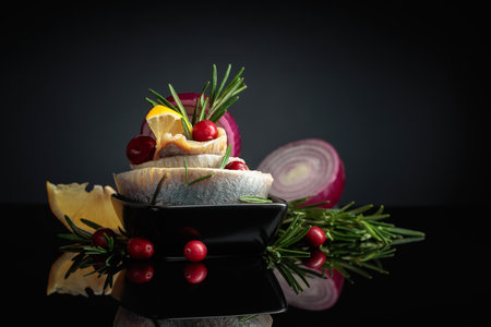 Herring fillet in oil with lemon, red onion, and rosemary garnished with cranberries. Black dish...