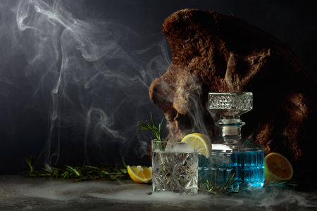Cocktail Gin-tonic with lemon and rosemary in a crystal glass. Smoked rosemary old-fashioned cocktail on a table. In the background old snag.の写真素材