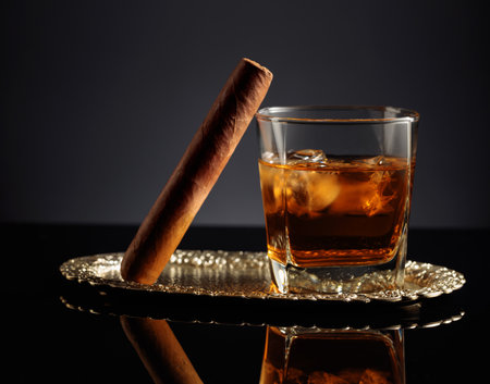 Whiskey with ice and cigar on a black reflective background.の写真素材