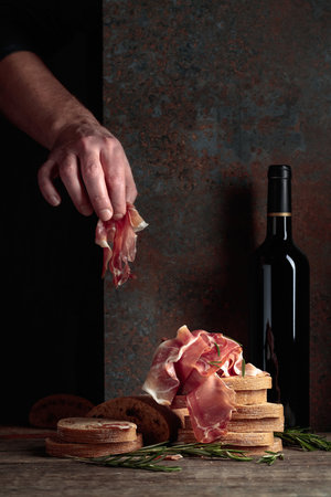 Prosciutto with bread and rosemary on an old wooden table. Traditional Mediterranean food.の写真素材