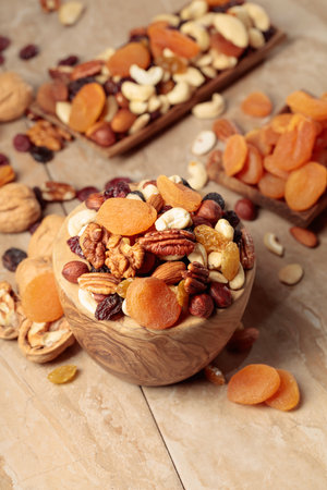 Dried fruits and nuts on a beige ceramic table. The mix of nuts, apricots, and raisins in a wooden bowl.の写真素材