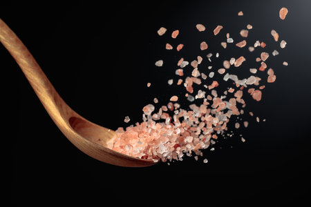 Pink Himalayan salt is poured with a wooden spoon. Himalaya salt on a dark background. Copy space.の写真素材
