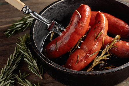 Roasted Bavarian sausages with rosemary in an old black pan.の写真素材