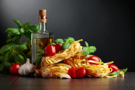 Homemade raw pasta with olive oil, tomato, garlic, and basil on a black background.の写真素材