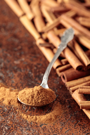 Cinnamon powder in a spoon and cinnamon sticks on a brown background.の写真素材