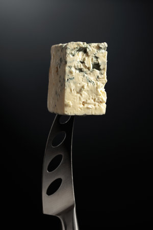 Blue cheese on a knife. Black background.