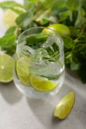 Mojito with ice, lime, and mint on a white stone table. Cold refreshing drink with natural ice in a misted glass.の写真素材