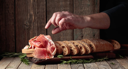 Prosciutto with bread and rosemary on an old wooden table. Traditional Mediterranean food.の写真素材