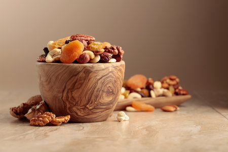 Dried fruits and nuts on a beige ceramic table. The mix of nuts, apricots, and raisins in a wooden bowl. Copy space.の写真素材