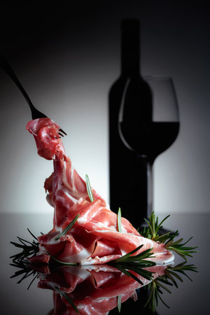 Italian prosciutto or Spanish jamon with rosemary and red wine on a black background.の写真素材