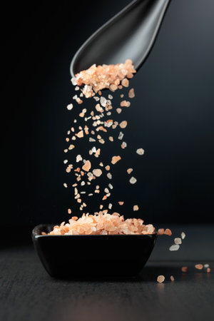 Pink salt is poured into a small black bowl. Himalayan salt on a black background.の写真素材