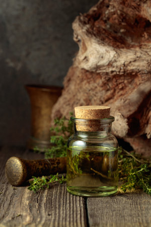 Bottle of thyme essential oil with fresh thyme twigs on an old wooden table.の写真素材