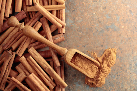Cinnamon powder in a wooden spoon and cinnamon sticks on a rusty metal background. Top view. Copy space.の写真素材