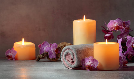 Towels, orchid flowers, and burning candles on a grey background. Spa concept with copy space.