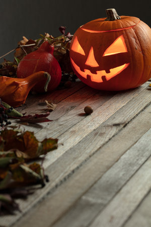 Halloween pumpkin head jack lantern with dried-up leaves. Halloween holidays art design, celebration. Carved Halloween pumpkin with burning candle.の写真素材