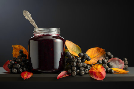 Chokeberry jam and fresh berries with leaves on a black background.の写真素材