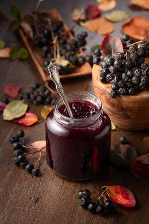 Chokeberry jam and fresh berries with leaves on an old wooden table.の写真素材