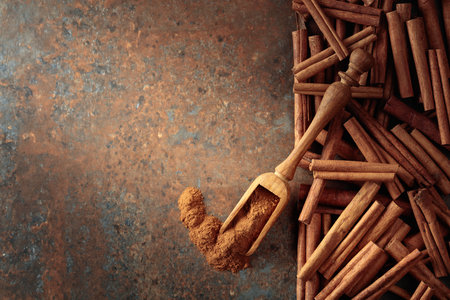 Cinnamon powder in a wooden spoon and cinnamon sticks on a rusty metal background. Top view. Copy space.の写真素材