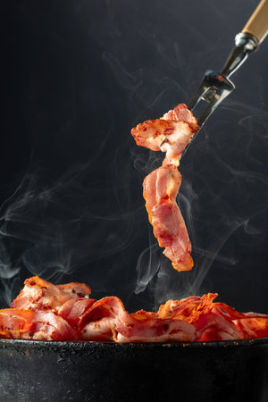 Fried steaming bacon slices on a black background. Copy space.の写真素材