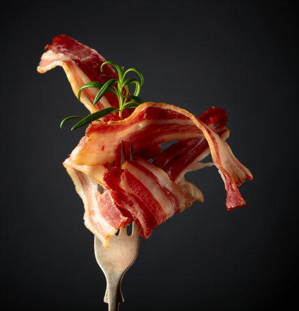 Slices of tasty fried bacon garnished with rosemary on a black background.