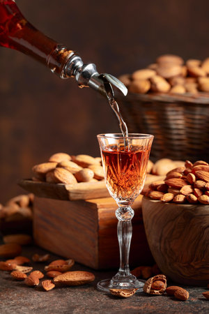 Italian liqueur Amaretto with almonds nuts on a vintage table. Liqueur is poured from a bottle into a glass.の写真素材