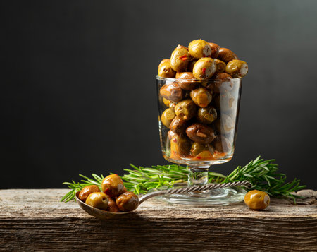 Spicy olives in a glass bowl. Bowl with preserved olives and rosemary twigs on a wooden table.の写真素材