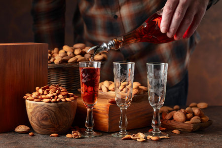 Italian liqueur Amaretto with almonds nuts on a vintage table. Liqueur is poured from a bottle into a glass.の写真素材