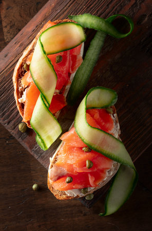 Sandwiches with smoked trout, cream cheese, fresh cucumber, and capers on an old cutting board. Top view.の写真素材