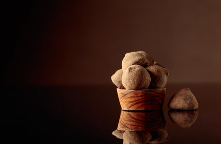 Chocolate truffles in small wooden dish sprinkled with cocoa powder. Black reflective background. Copy space.の写真素材