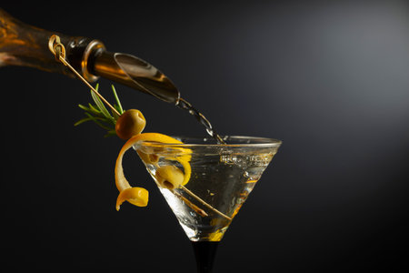 Classic dry martini cocktail with green olives, lemon peel, and rosemary on a black background. Free space for your text.の写真素材