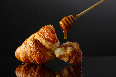 Fresh baked croissant with honey on a black reflective background. Copy space.の写真素材