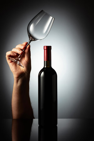 Unopened bottle of red wine and hand with wine glass. Concept of the wine theme.