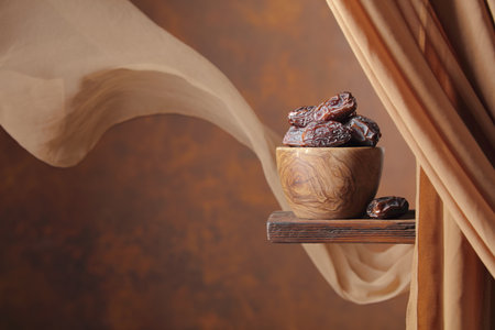 Medjool dates in wooden dish on a brown background. In the background there is a beige curtain...