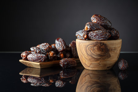 Dates in wooden dish on a black reflective background.の写真素材