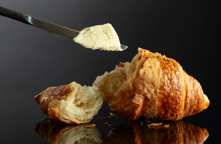 Fresh baked croissant with butter on a black reflective background.の写真素材