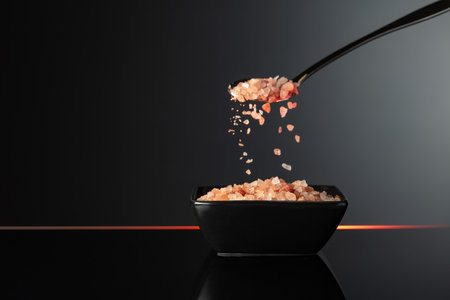 Pink Himalayan salt in a small black ceramic bowl on a black reflective background. Copy space.の写真素材
