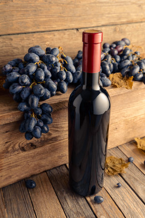 Bottle of red wine with blue grapes on an old wooden table.の写真素材