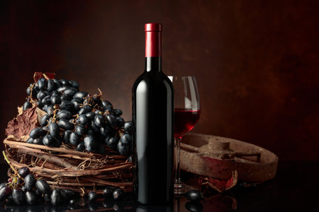 Glass and bottle of red wine with blue grapes on a black reflective background. Copy space.の写真素材