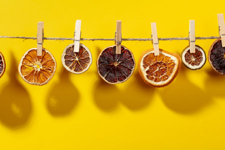 Orange, lemon and lime slices are dried on a line. Bright sunlight and shadows on a yellow background. Copy space.の写真素材