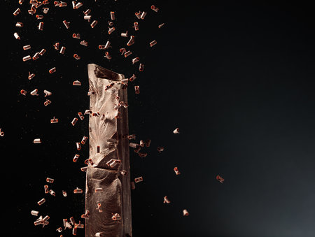 Large piece of dark chocolate and falling chocolate crumbs on a black background.の写真素材