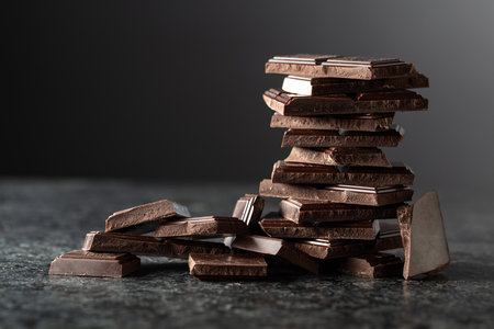 Broken bitter chocolate bar on a black background. Copy space.