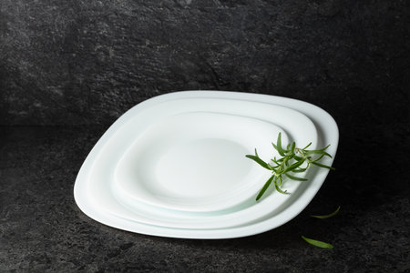 Empty white plates with rosemary on a black stone background with copy space. Place your product on...