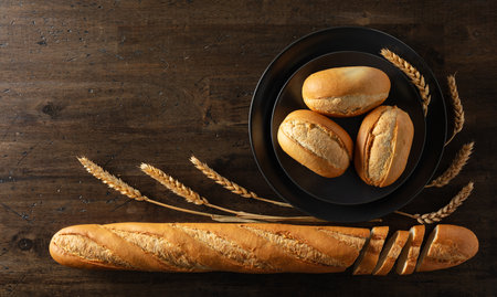 Baguette, French buns, and wheat ears on an old wooden table. Top view. Copy space.