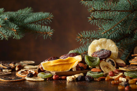 Dried tropical fruits with various nuts and raisins on an old brown table. Sweet tropical fruits and Christmas tree on a kitchen table.の写真素材