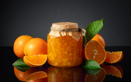 Orange jam in glass jar and fresh fruits. Sweet confiture on a black reflective background.の写真素材