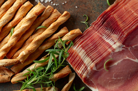 Prosciutto with bread sticks and rosemary on a brown rusty background. Top view.