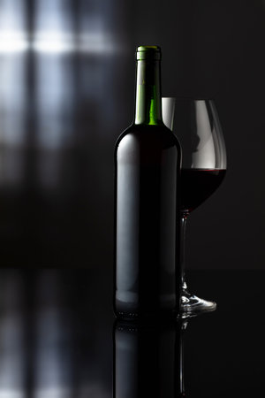 Glass and bottle of red wine on a black reflective background. Frontal view with space for your text.の写真素材