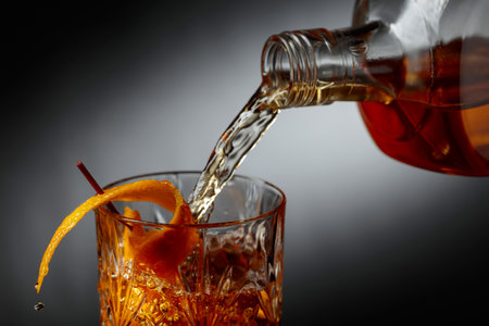 Whiskey or bourbon pouring into a crystal glass. Old-fashioned cocktail classic bourbon whiskey and bitters, garnished with orange peel.の写真素材